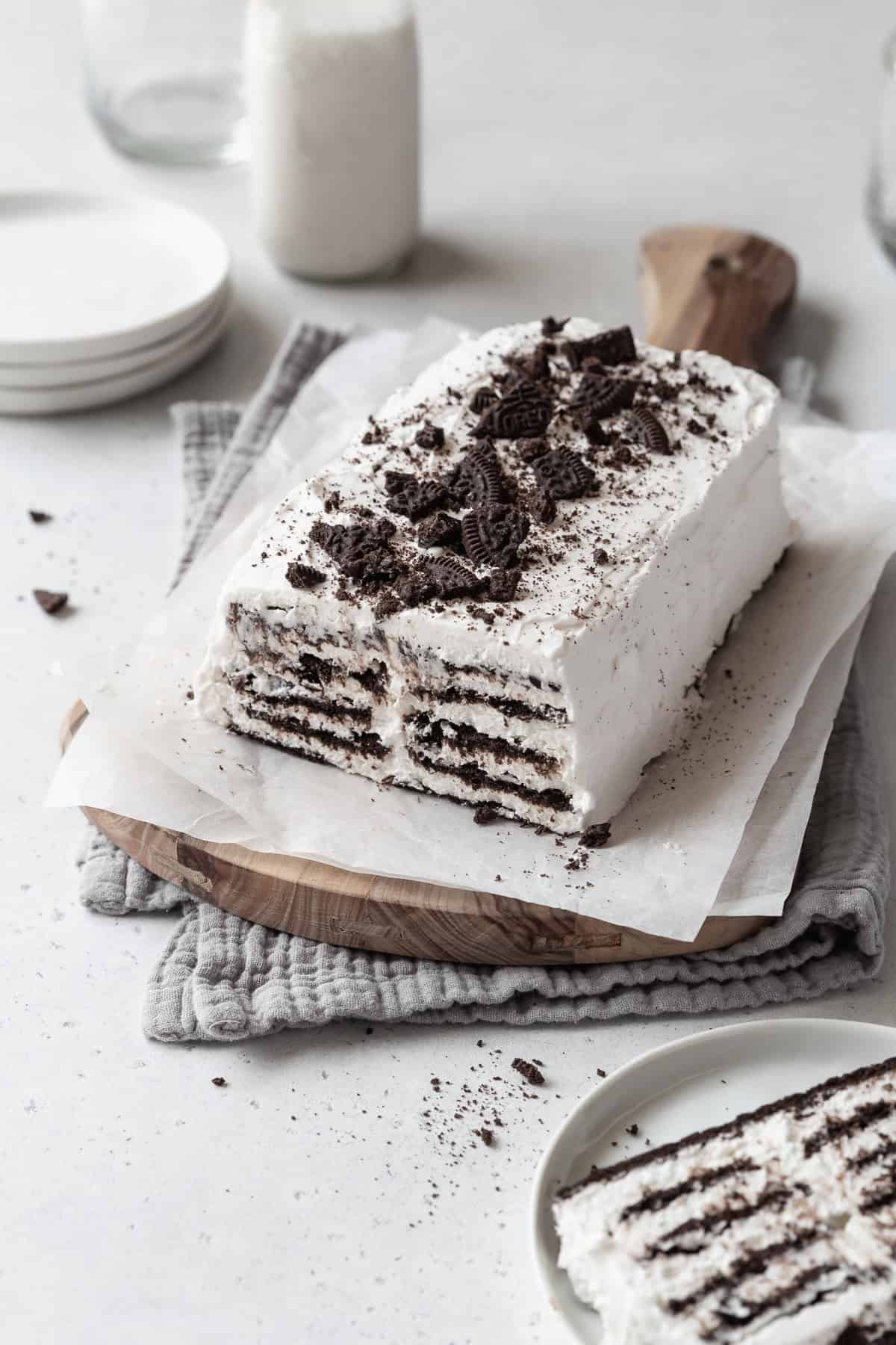 A loaf of icebox cake with cookie crumbs on top on a parchment paper lined wooden board. 
