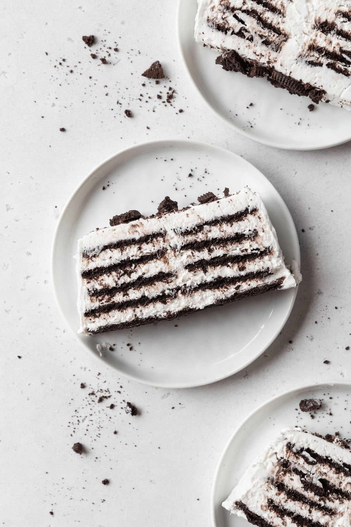 Three slices of icebox cake on white plates on a light grey surface.