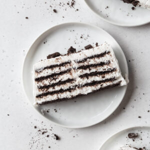 A slice of icebox cake on a white plate with Oreo crumbs.