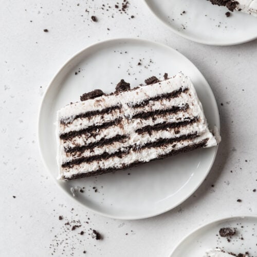 A slice of icebox cake on a white plate with Oreo crumbs.