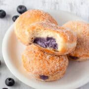 Blueberry donuts on a plate filled with blueberry cream cheese filling.