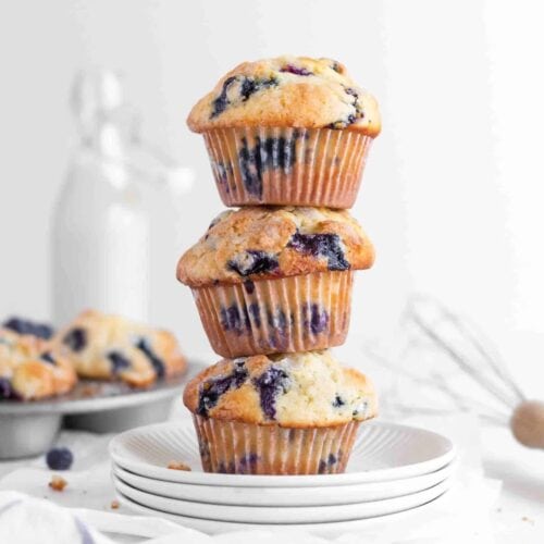 A stack of three blueberry muffins on white plates.