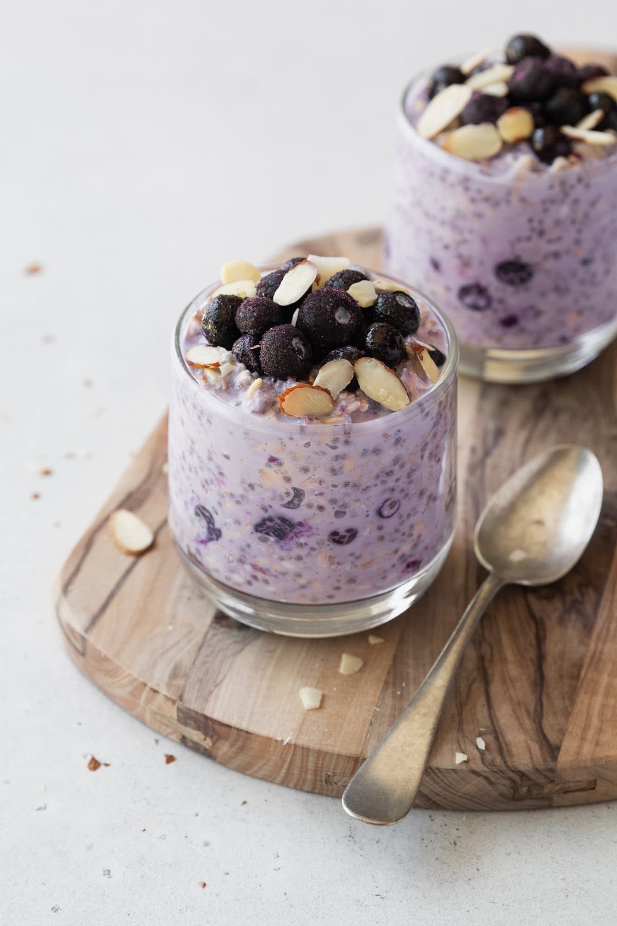 Two glass of blueberry overnight oats on a wooden board with a spoon.