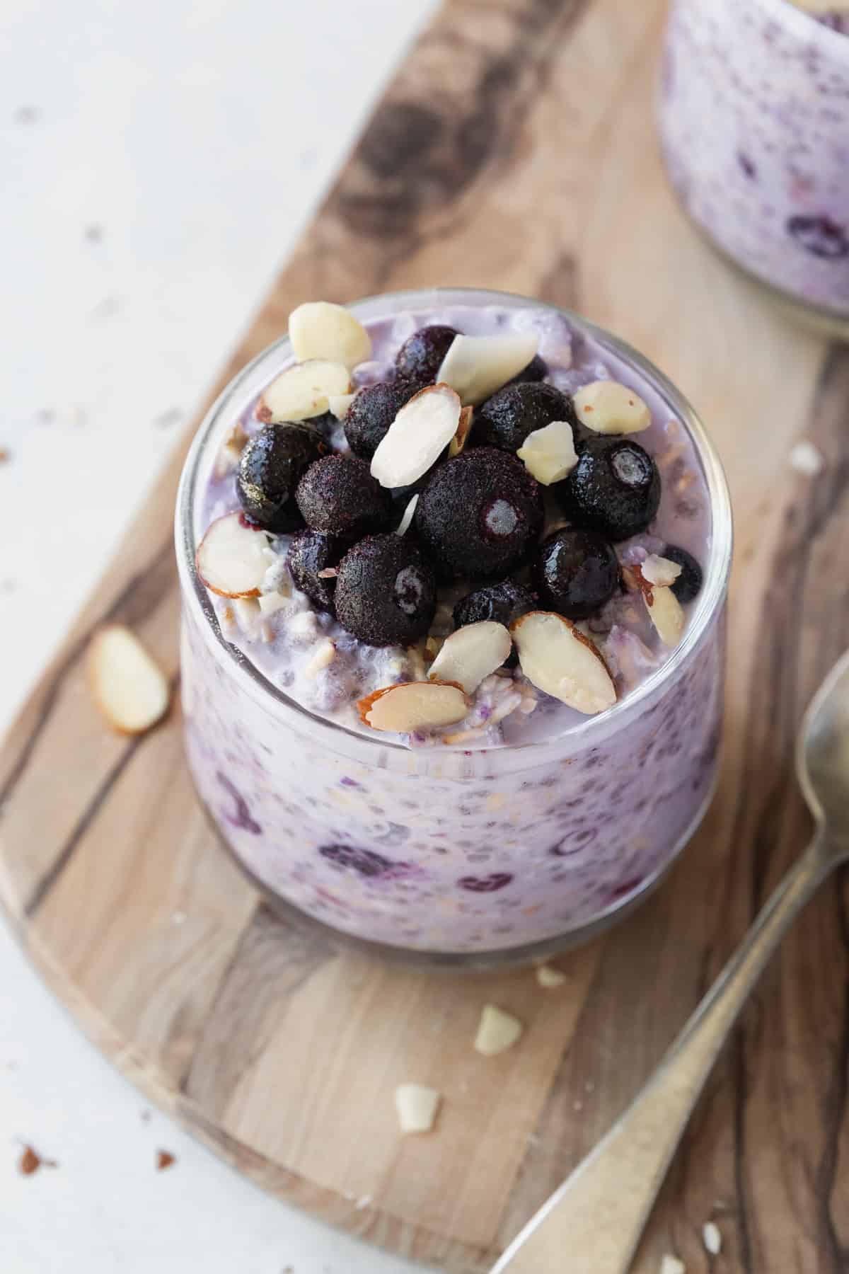 Frozen blueberries and sliced almonds on a glass of overnight oats.