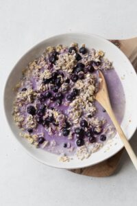 Blueberry overnight oats being mixed together in a white bowl with a wooden spoon.