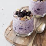 Blueberry overnight oats in a glass topped with frozen blueberries and sliced almonds.