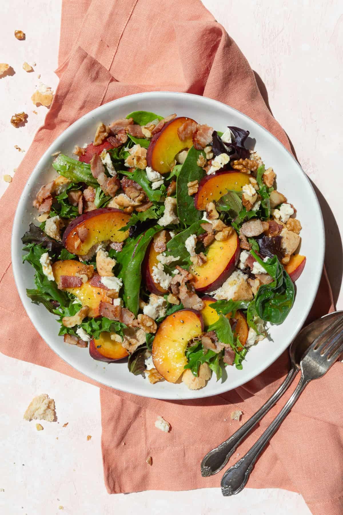 Peach salad with cheese and bacon in a white bowl on a pink linen.