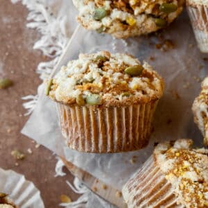 A gluten free pumpkin muffin with streusel topping and pumpkin seeds on a piece of parchment paper.