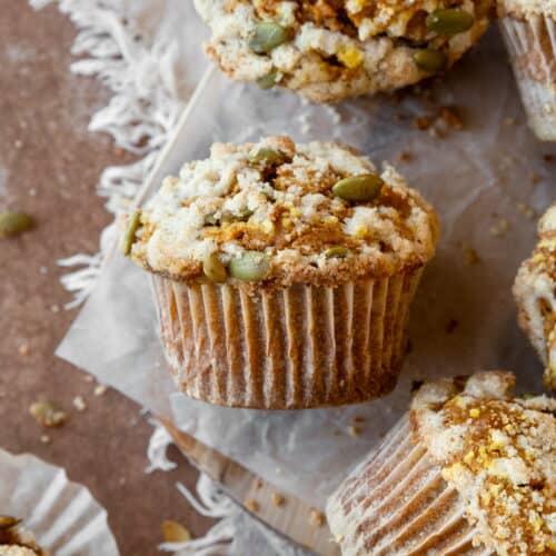 A gluten free pumpkin muffin with streusel topping and pumpkin seeds on a piece of parchment paper.