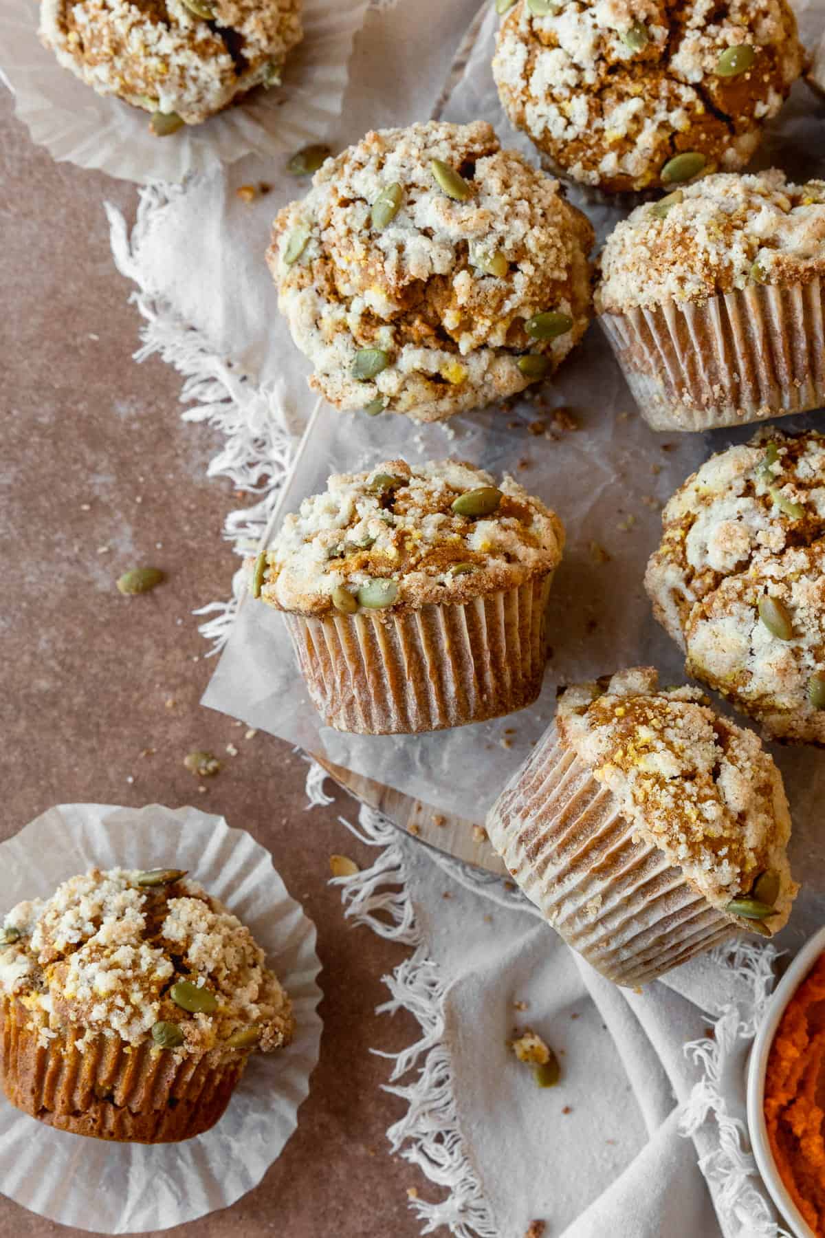 Gluten free pumpkin muffins with streusel scattered on a piece of parchment paper, with some on the side.