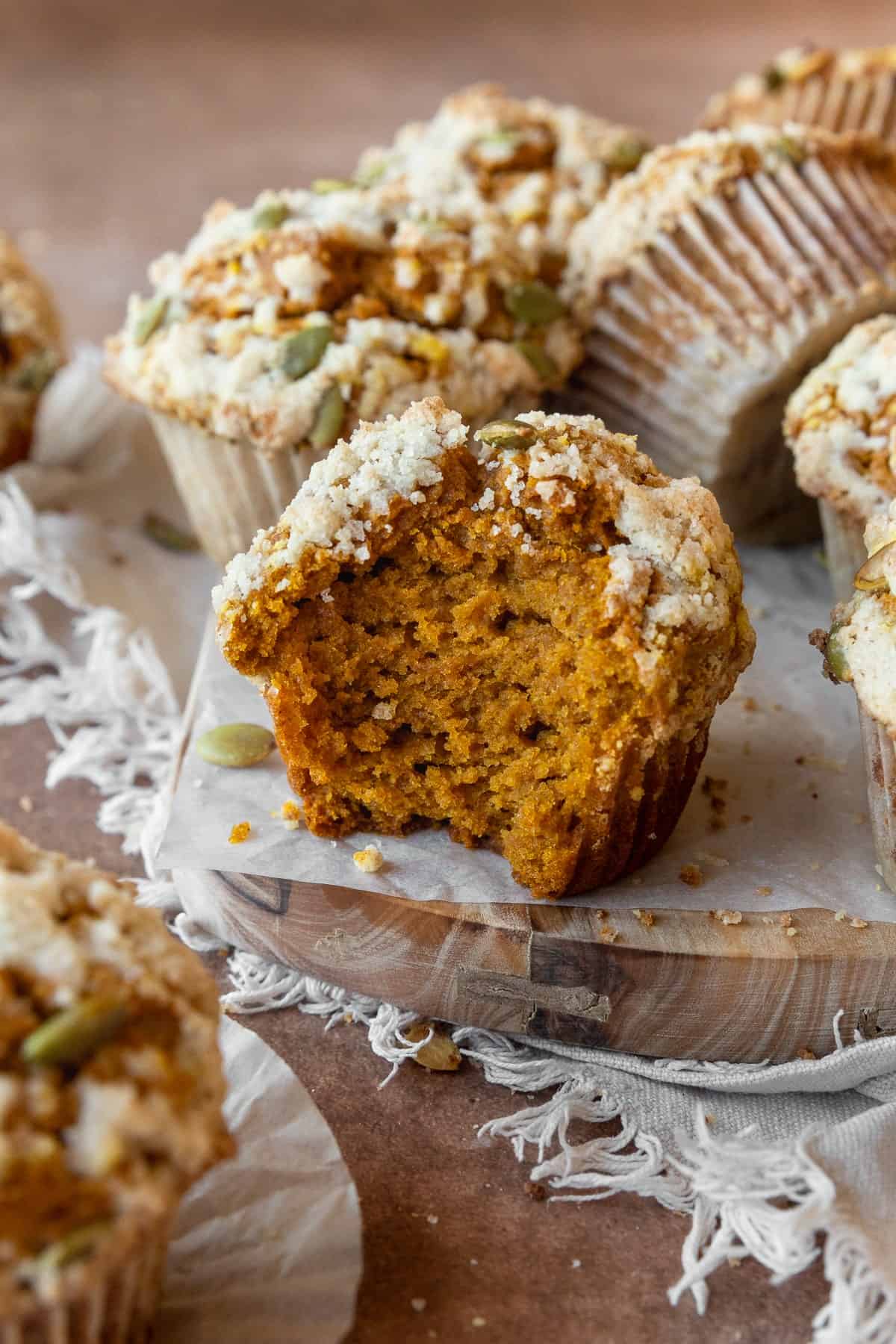 A gluten-free pumpkin muffin with a bite taken out, with more muffins around it.