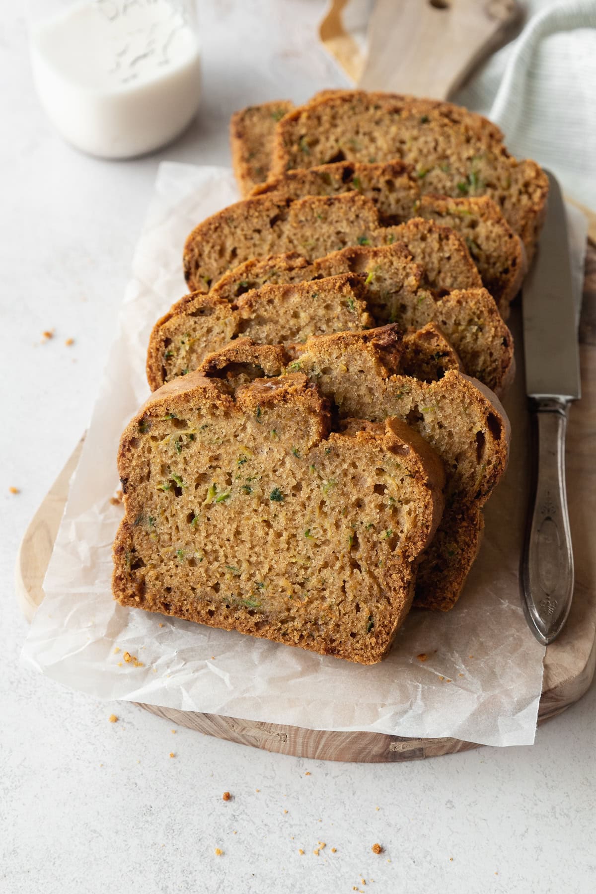 Slices of gluten free zucchini bread on a parchment lined wooden board, with a silver knife beside it.