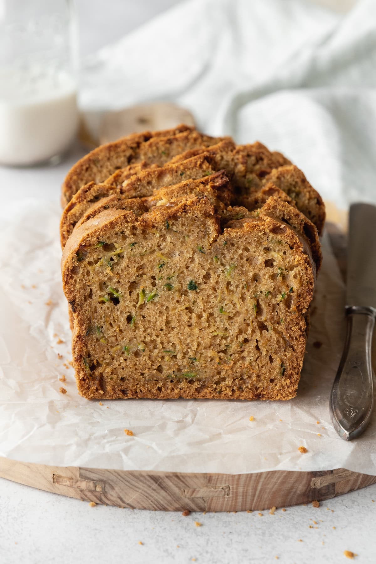 A sliced zucchini loaf on a piece of parchment paper, with a bottle of milk in the background.