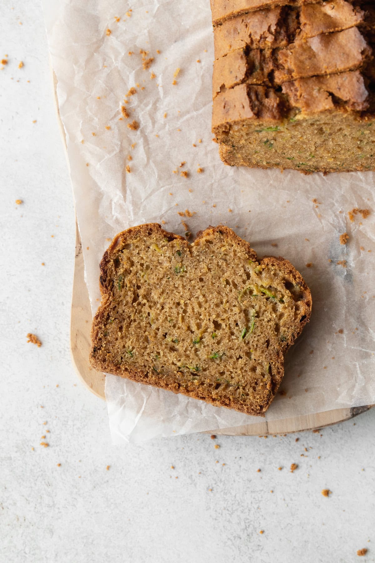 A slice of gluten free zucchini bread on a parchment-lined wooden board, with the more slices to the side.