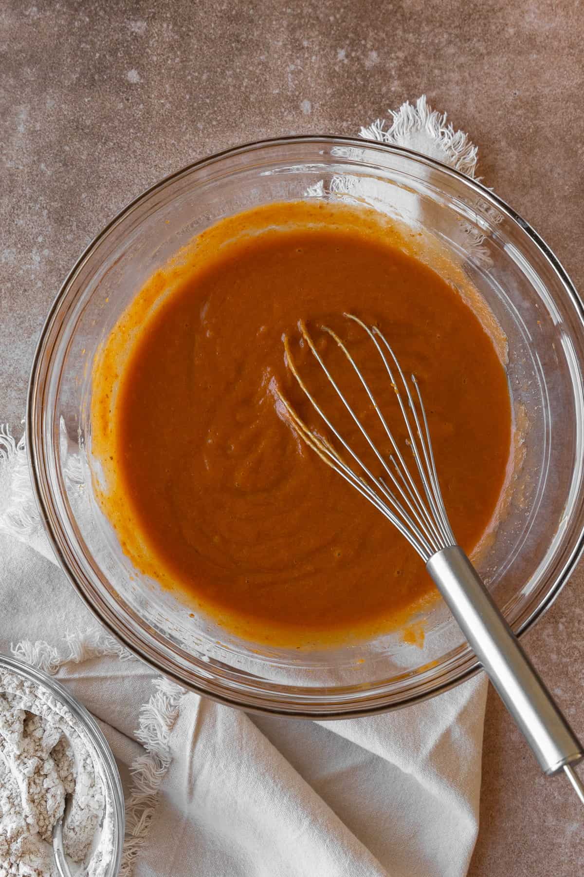 Wet ingredients for pumpkin muffins in a glass bowl with a wire whisk.
