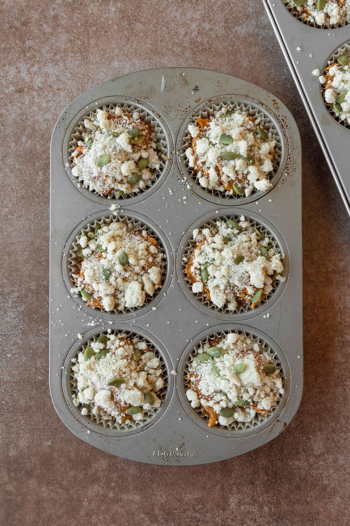 Pumpkin muffin batter topped with streusel topping in a muffin pan.
