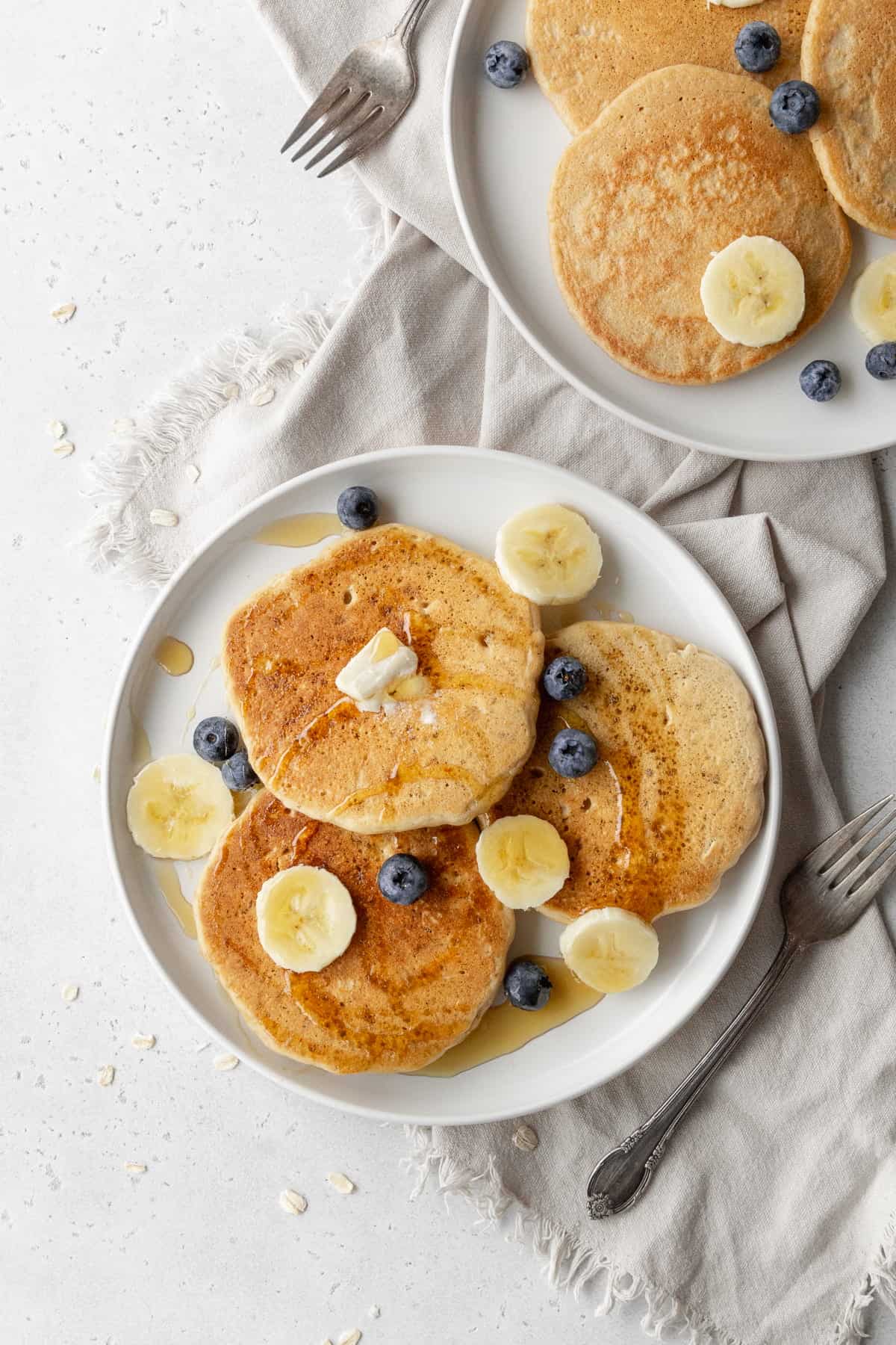 Two plates of pancakes with banana slices and blueberries.