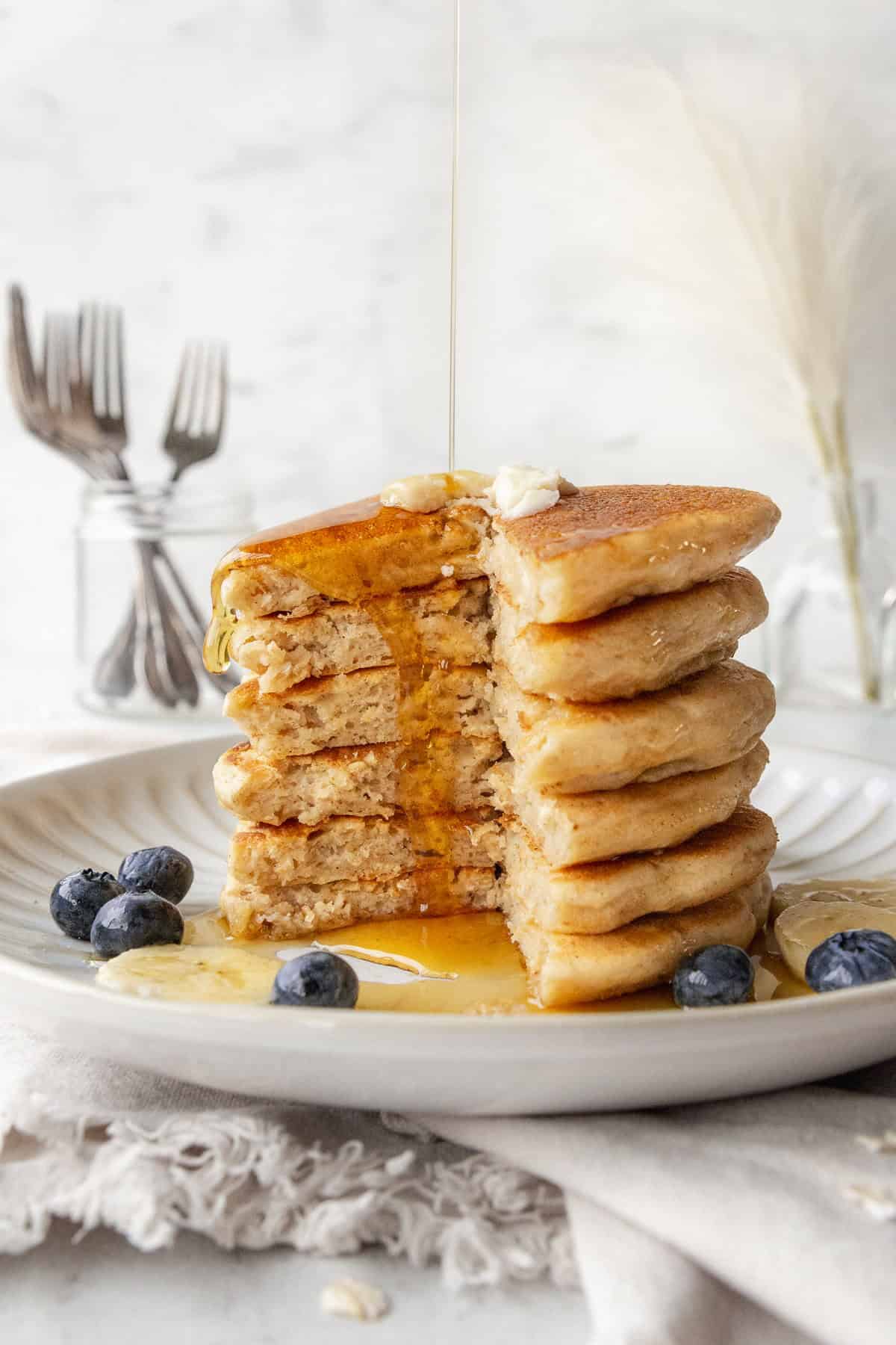 A stack of pancakes that's been cut into, with maple syrup being poured over.