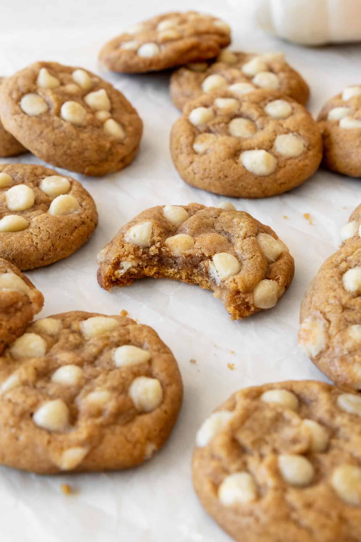 A bitten gluten free pumpkin cookie surrounded by more cookies on a piece of parchment paper.