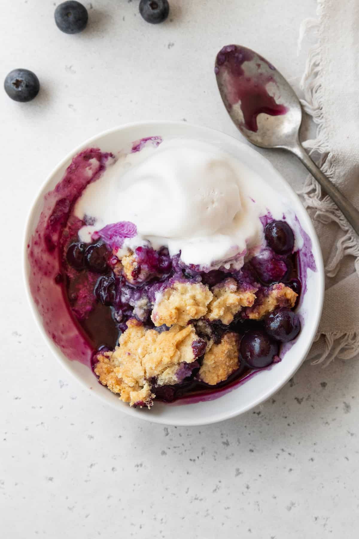 Semi-eaten blueberry cobbler with melting ice cream in a white bowl.