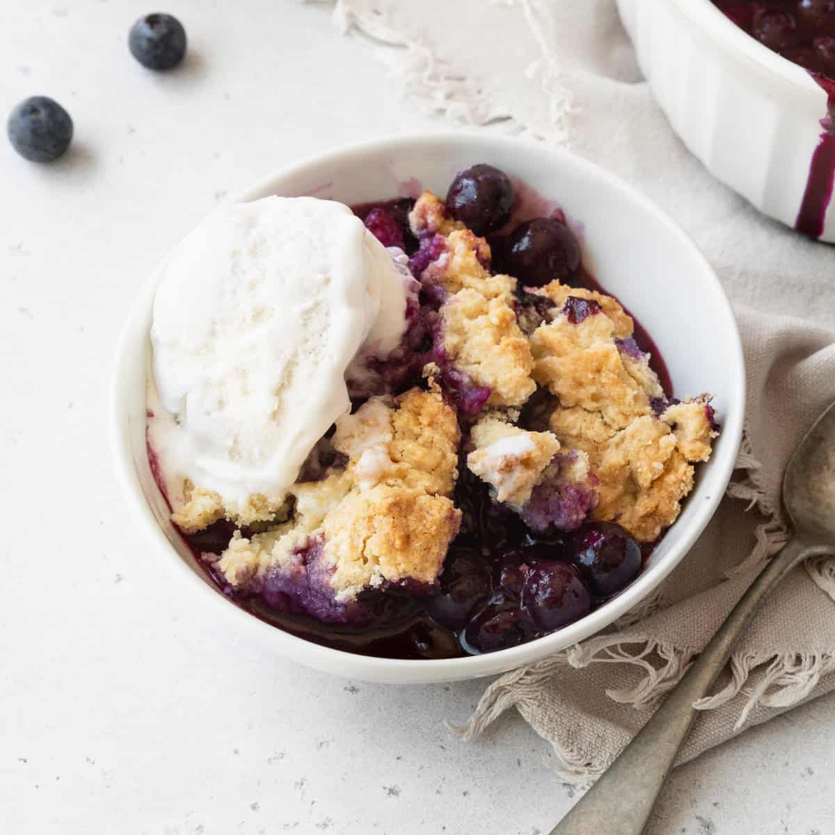 A bowl of blueberry cobbler and a scoop of vanilla ice cream.